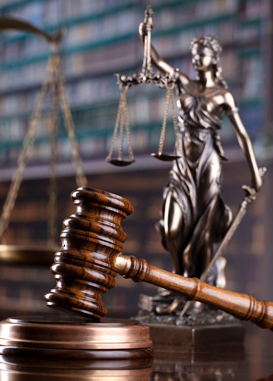 Statue of Lady Justice holding scales, alongside a gavel on a wooden table, symbolizing law and justice concepts.